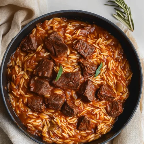 Rustic serving of saucy orzo and beef, with rosemary sprig nearby.