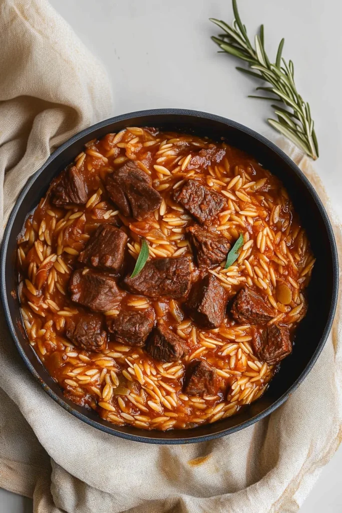 Rustic serving of saucy orzo and beef, with rosemary sprig nearby.