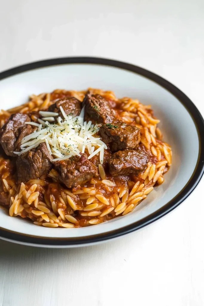 Hearty bowl of orzo pasta coated in tomato sauce with tender beef chunks.