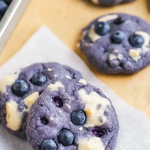 Round purple cookies with embedded blueberries on parchment paper.