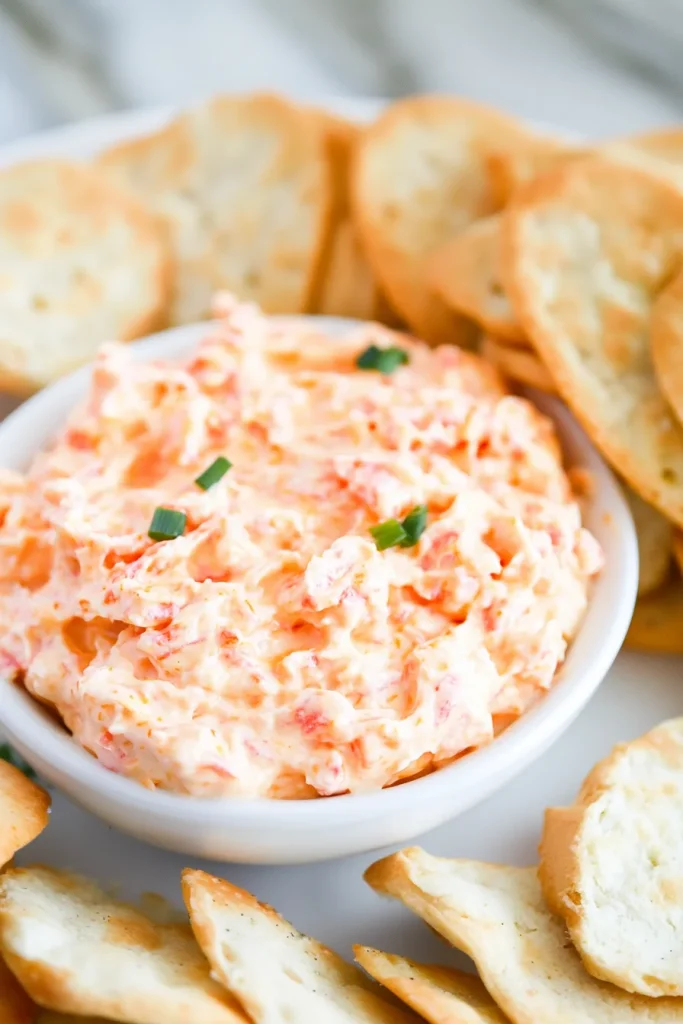 Bowl of creamy orange dip with herbs sprinkled on top.