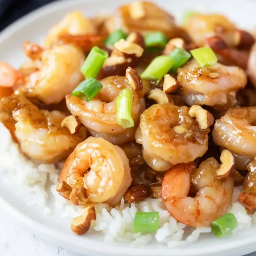 Shrimp coated in a glossy sauce, served over rice with chopped green onions and nuts.