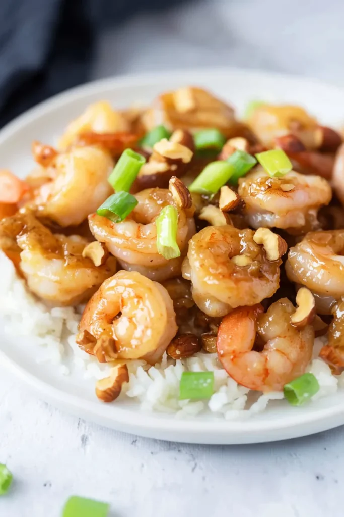 Shrimp coated in a glossy sauce, served over rice with chopped green onions and nuts.