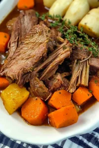 White plate of slow-cooked beef and vegetables on a checkered cloth.