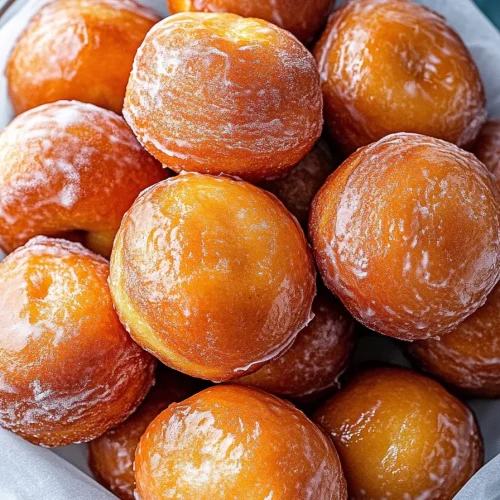 Glazed golden doughnuts stacked in a glass bowl.