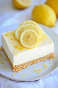Fresh lemon cheesecake photographed with whole lemons in the background.