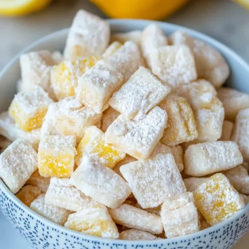Decorative bowl filled with lemon candy pieces beside fresh lemons.