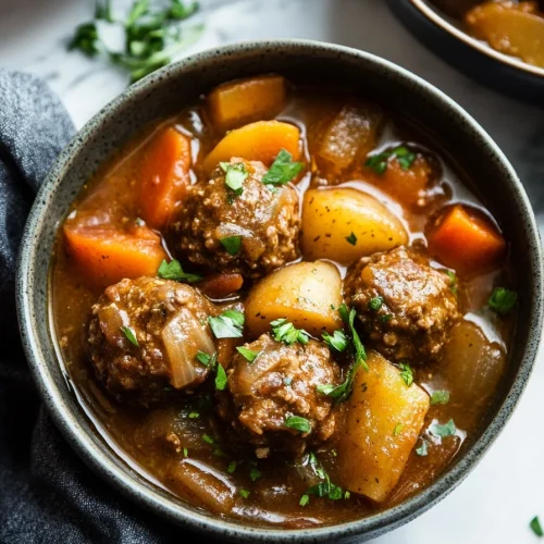 A rustic bowl filled with tender meatballs, baby potatoes, and carrots in a rich brown gravy, garnished with fresh parsley.