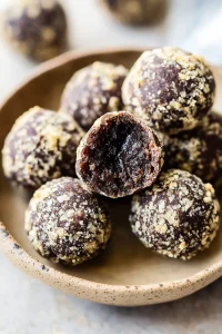 Round chocolate truffles coated in crushed nuts, arranged in a ceramic bowl.