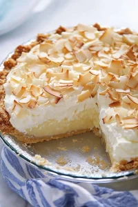 Rich custard pie topped with fluffy cream and sprinkled coconut, captured in soft light.
