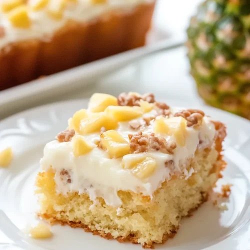 Slice of light yellow sponge cake topped with creamy frosting, pineapple chunks, and nuts.