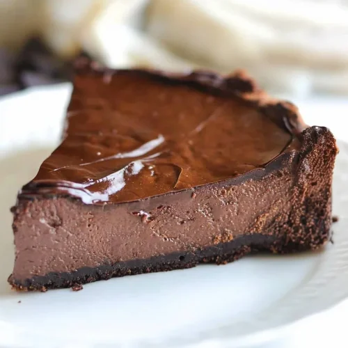 Slice of dense chocolate cheesecake with glossy ganache topping.