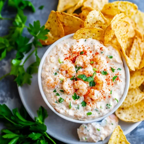 Creamy dip topped with shrimp pieces, green onions, and paprika, surrounded by tortilla chips.