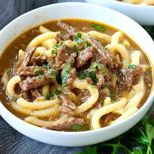 Close-up of thick noodles coated in savory gravy, garnished with herbs.