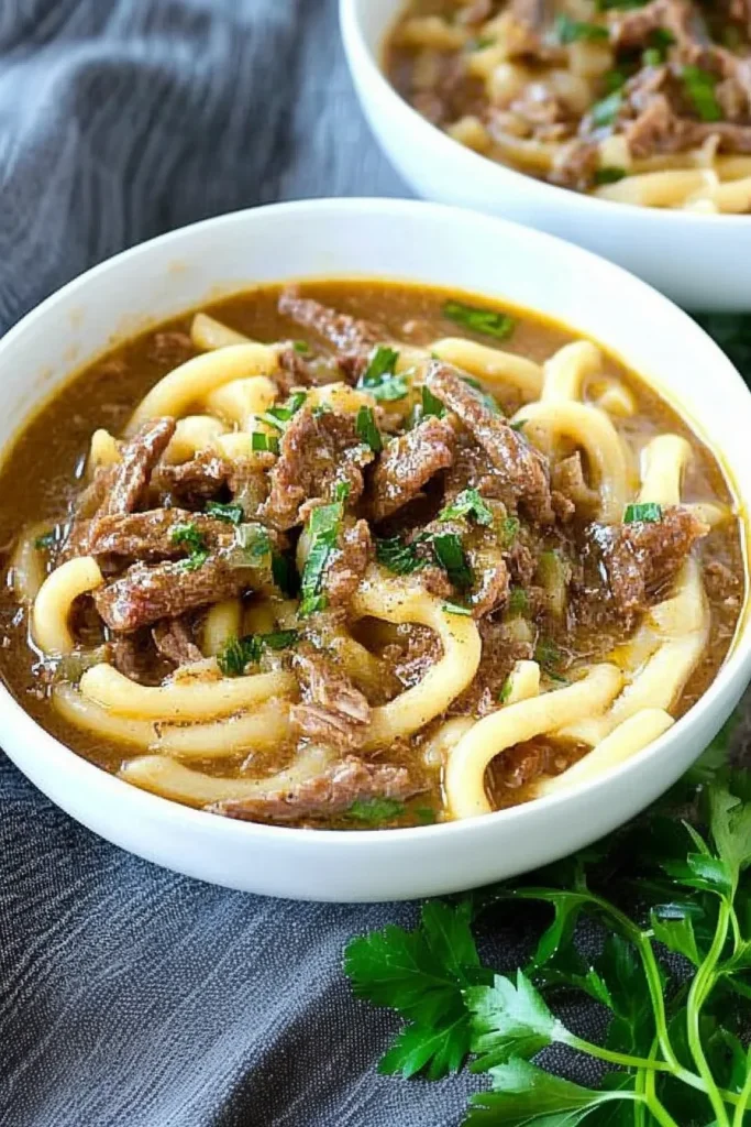 Close-up of thick noodles coated in savory gravy, garnished with herbs.