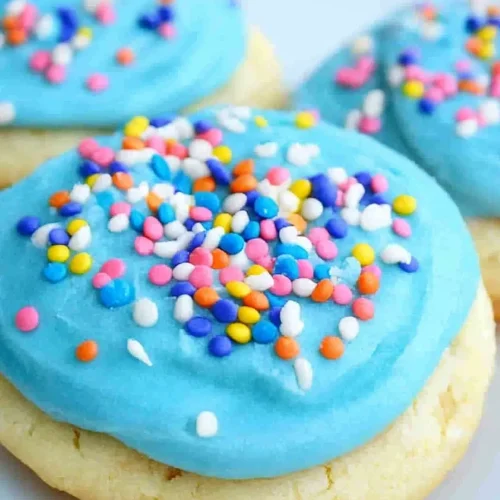 Close-up of frosted cookies decorated with pink, yellow, and blue sprinkles.