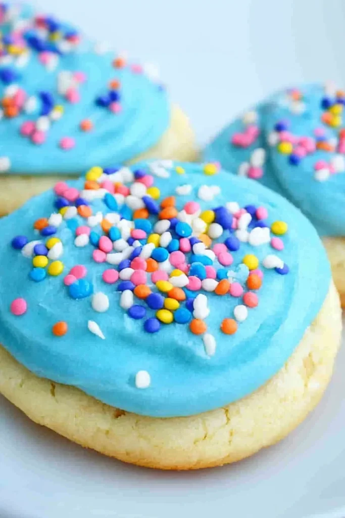 Close-up of frosted cookies decorated with pink, yellow, and blue sprinkles.