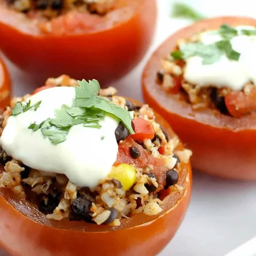 Bright red tomatoes filled with beans, corn, and couscous, topped with sour cream and herbs.