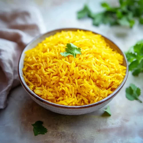 Golden rice garnished with fresh herbs, presented in a simple bowl.