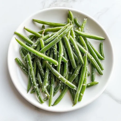 Glossy green beans piled on a white plate, sprinkled with coarse salt.