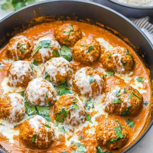 Pan of saucy meatballs served alongside a bowl of white rice