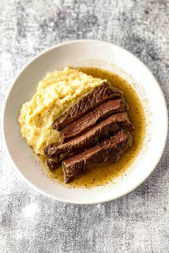 White bowl filled with beef and gravy, garnished with fresh herbs.
