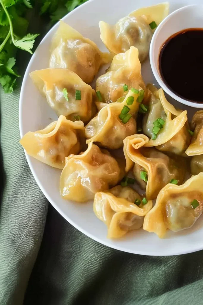 Steamed dumplings arranged neatly on a white plate with dipping sauce.