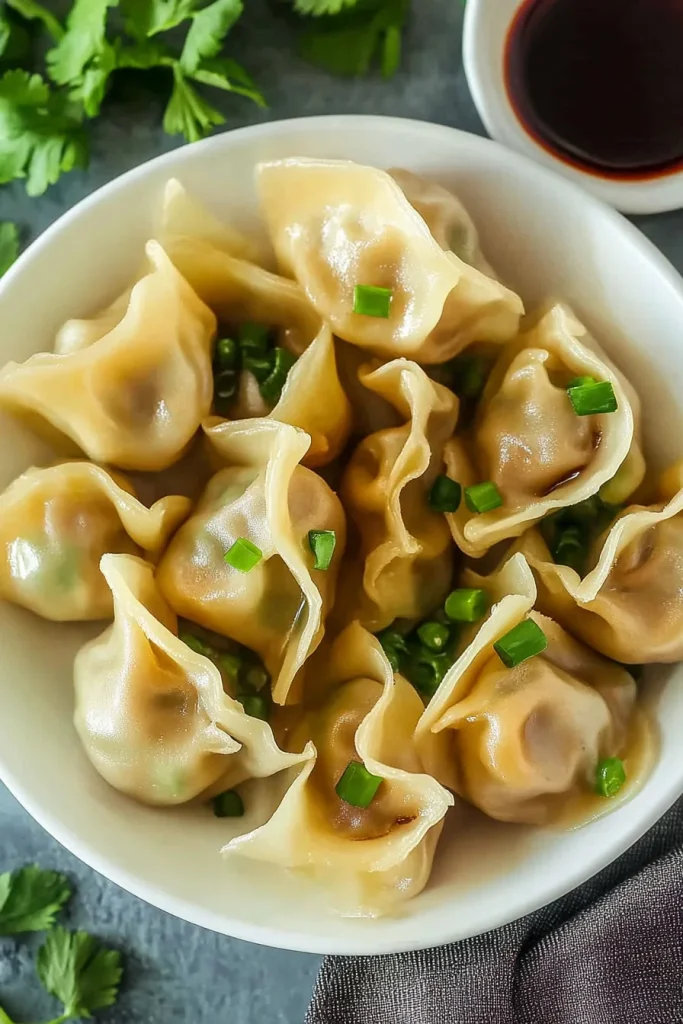 Plate of dumplings beside a small bowl of dark soy sauce.