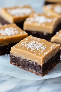 Dense chocolate bars with glossy caramel topping, styled simply on parchment paper.